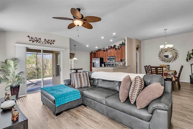 living room with ceiling fan with notable chandelier, vaulted ceiling, and light wood-type flooring