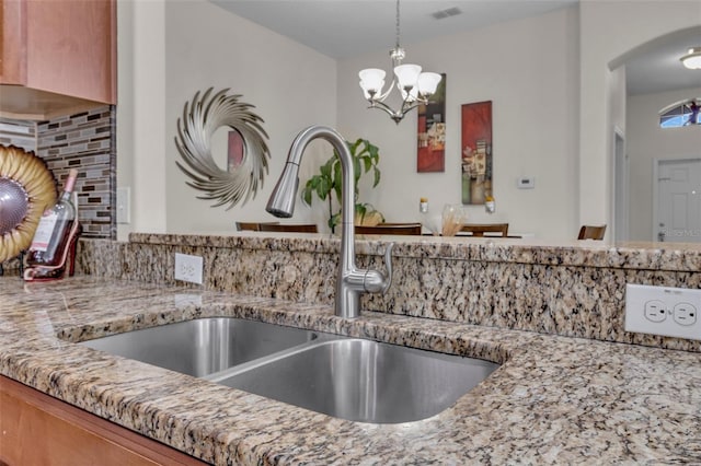 kitchen featuring light stone countertops, tasteful backsplash, sink, decorative light fixtures, and an inviting chandelier