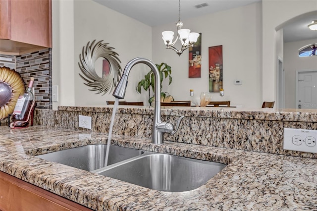 interior details featuring sink, hanging light fixtures, light stone countertops, tasteful backsplash, and a notable chandelier