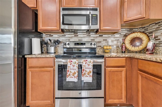 kitchen with light stone countertops, appliances with stainless steel finishes, and backsplash