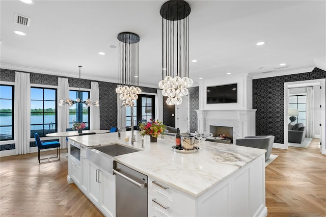 kitchen with white cabinets, light parquet flooring, an island with sink, pendant lighting, and a water view