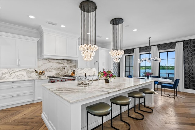 kitchen featuring an inviting chandelier, a center island with sink, a water view, decorative light fixtures, and white cabinetry