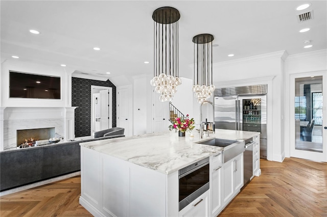 kitchen with white cabinetry, decorative light fixtures, a center island with sink, light parquet flooring, and appliances with stainless steel finishes