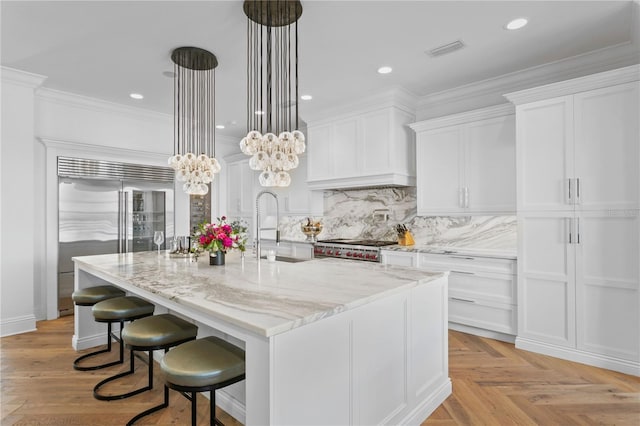 kitchen with stainless steel appliances, white cabinetry, hanging light fixtures, and an island with sink