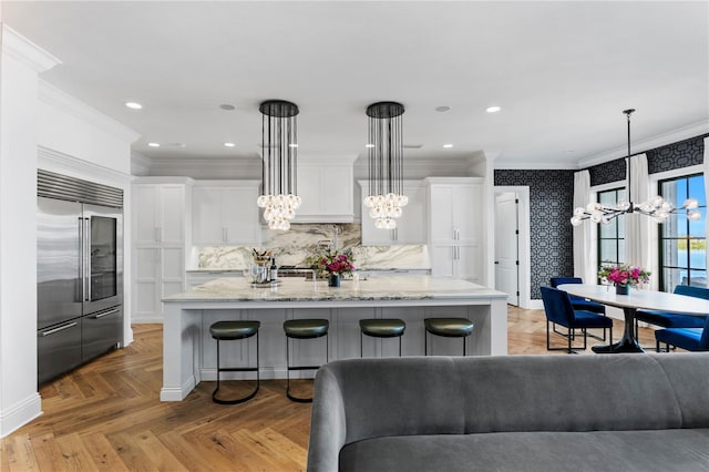 kitchen with white cabinetry, built in refrigerator, an island with sink, decorative light fixtures, and light parquet flooring