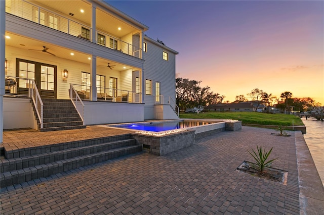 patio terrace at dusk featuring an in ground hot tub, a balcony, and ceiling fan