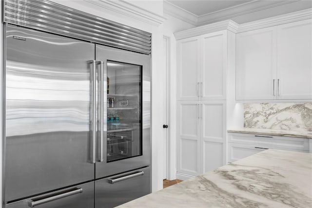 kitchen with white cabinets, ornamental molding, light stone counters, and built in fridge