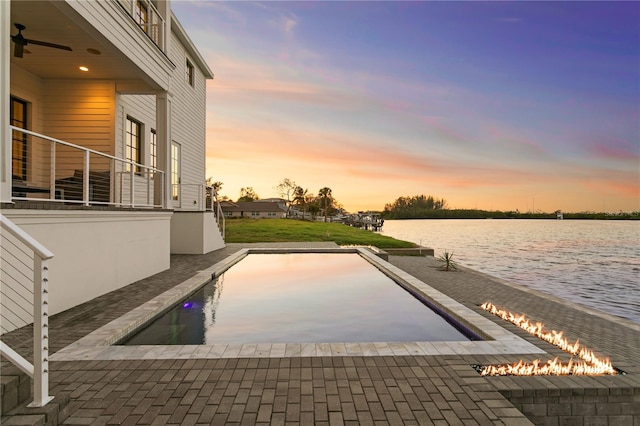 pool at dusk featuring a water view and ceiling fan