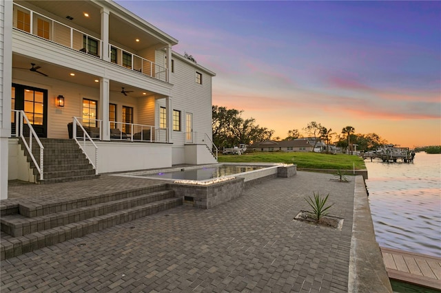 exterior space featuring an in ground hot tub, a balcony, a patio area, and a water view