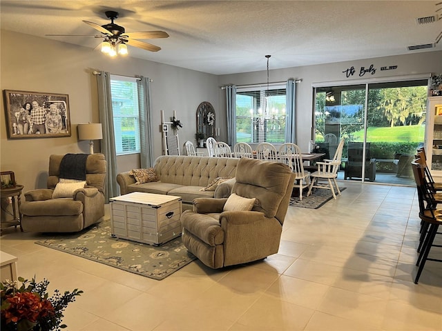 tiled living room with a textured ceiling, ceiling fan with notable chandelier, and a wealth of natural light