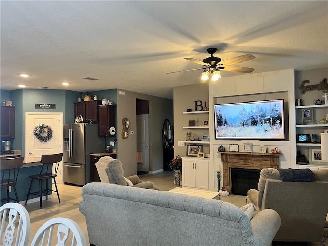 living room with built in shelves, ceiling fan, and a textured ceiling