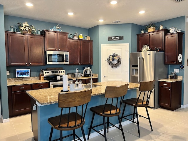 kitchen featuring sink, stainless steel appliances, a kitchen breakfast bar, a kitchen island with sink, and light tile patterned floors