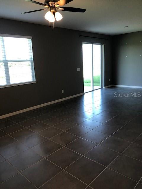 empty room featuring dark tile patterned flooring, plenty of natural light, and ceiling fan