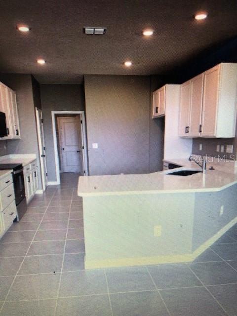 kitchen with stainless steel electric stove, white cabinetry, sink, and tile patterned floors