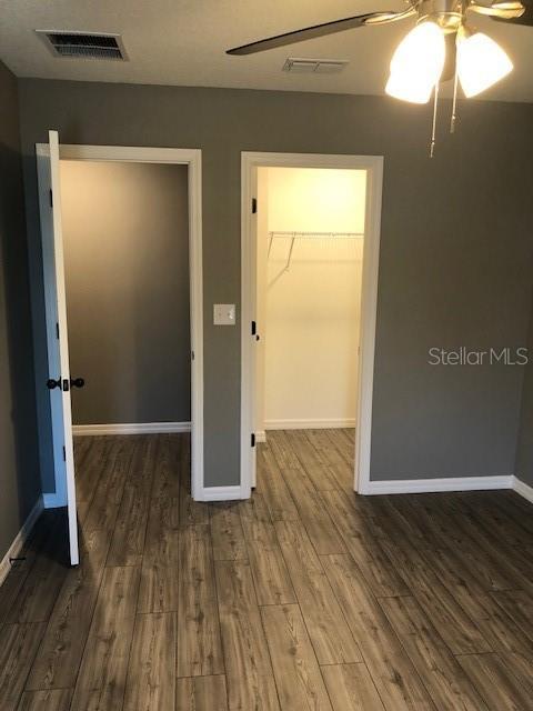 unfurnished bedroom with dark wood-type flooring, a walk in closet, ceiling fan, and a closet