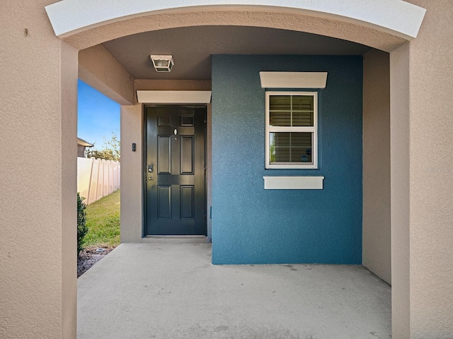 view of exterior entry with fence and stucco siding