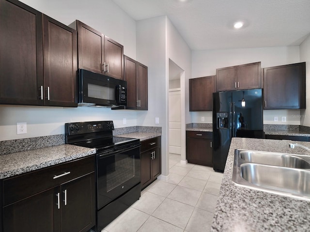 kitchen with light tile patterned floors, vaulted ceiling, a sink, dark brown cabinets, and black appliances