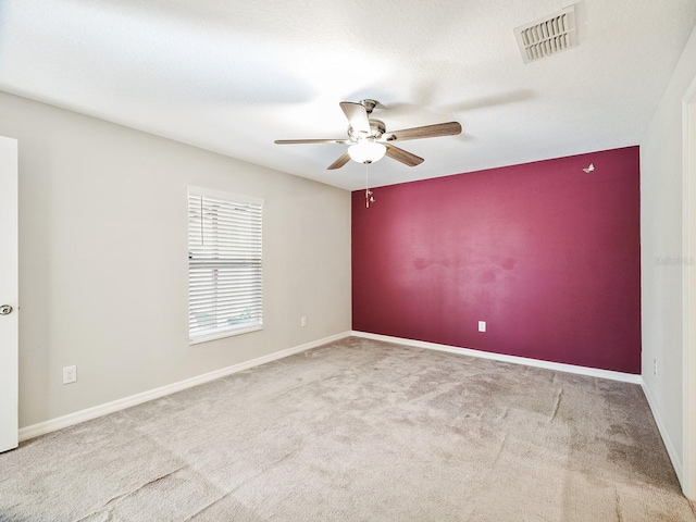 carpeted empty room with an accent wall, visible vents, ceiling fan, and baseboards