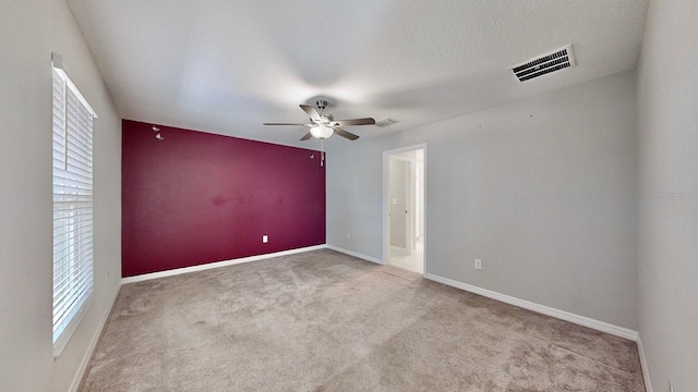 carpeted empty room with ceiling fan, a textured ceiling, visible vents, and baseboards