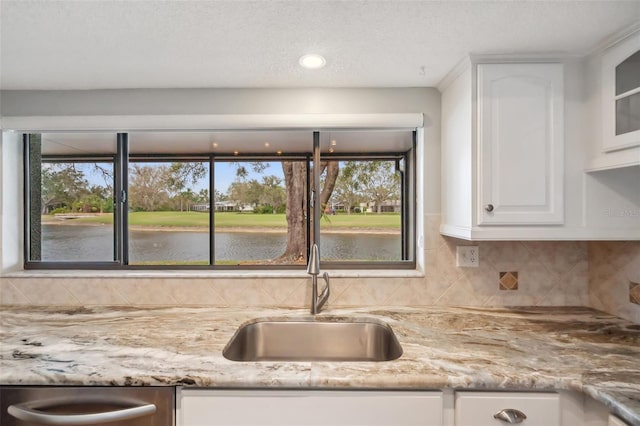 kitchen featuring a water view, a sink, white cabinets, backsplash, and light stone countertops