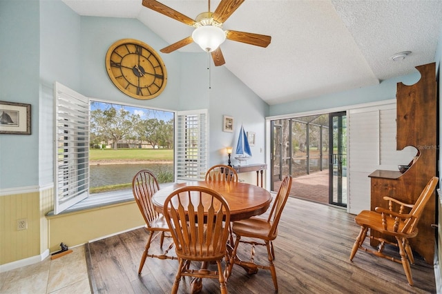 dining space with a textured ceiling, high vaulted ceiling, a wainscoted wall, and wood finished floors