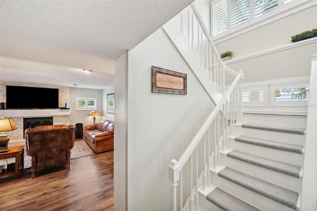 staircase with a textured ceiling, a fireplace, and wood finished floors