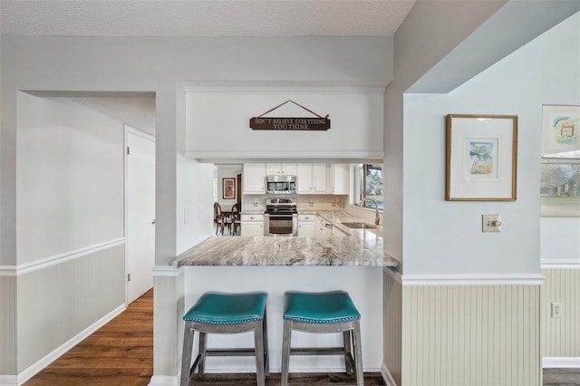 kitchen featuring a breakfast bar area, stainless steel appliances, a peninsula, a sink, and white cabinets