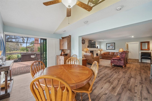 dining room featuring a fireplace, light wood-style floors, a ceiling fan, vaulted ceiling, and a textured ceiling