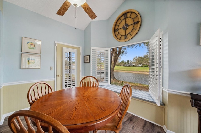 dining room with lofted ceiling, a water view, a ceiling fan, wainscoting, and wood finished floors