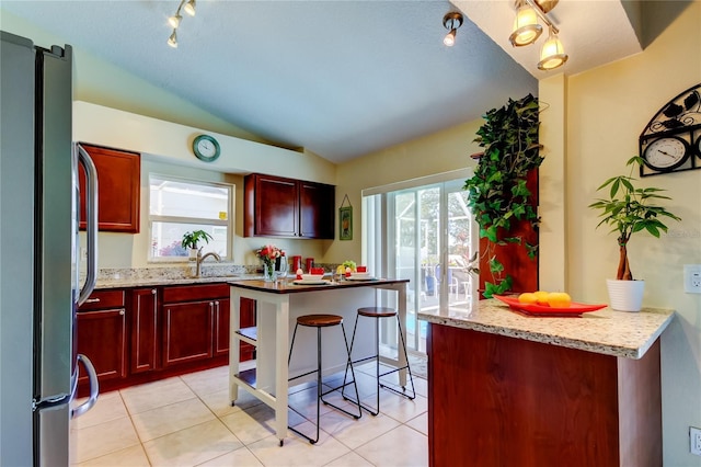 kitchen with lofted ceiling, stainless steel fridge, a kitchen breakfast bar, a center island, and light stone counters