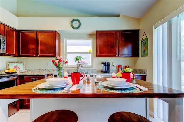 kitchen with wood counters, appliances with stainless steel finishes, vaulted ceiling, and a kitchen island