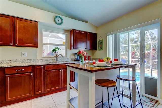 kitchen featuring sink, a breakfast bar area, light stone counters, vaulted ceiling, and light tile patterned floors