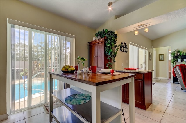 kitchen with wood counters, light tile patterned floors, vaulted ceiling, and a wealth of natural light