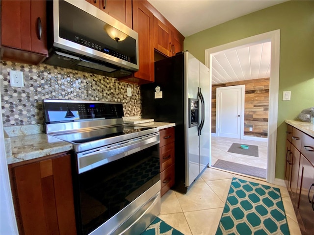 kitchen with wooden walls, decorative backsplash, light stone countertops, appliances with stainless steel finishes, and light tile patterned flooring