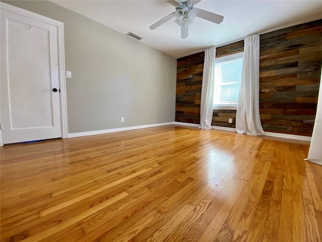 unfurnished room featuring ceiling fan, light hardwood / wood-style flooring, and wood walls