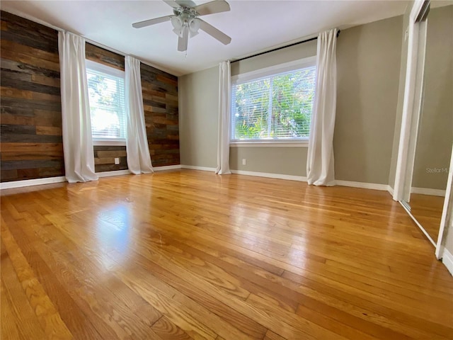 unfurnished room with a wealth of natural light, wooden walls, ceiling fan, and light hardwood / wood-style floors