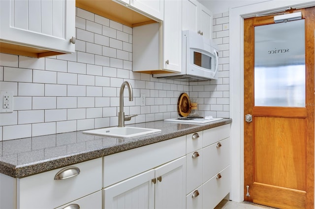 kitchen featuring white cabinets, decorative backsplash, light stone counters, and sink