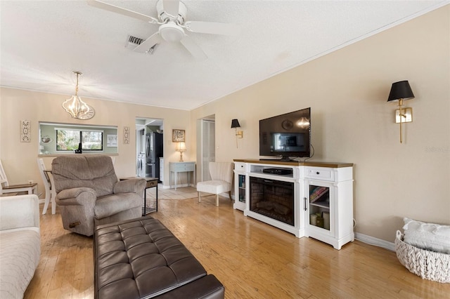 living room featuring ceiling fan with notable chandelier, light hardwood / wood-style floors, and a textured ceiling