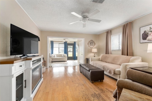 living room with ceiling fan, light hardwood / wood-style flooring, a healthy amount of sunlight, and a textured ceiling