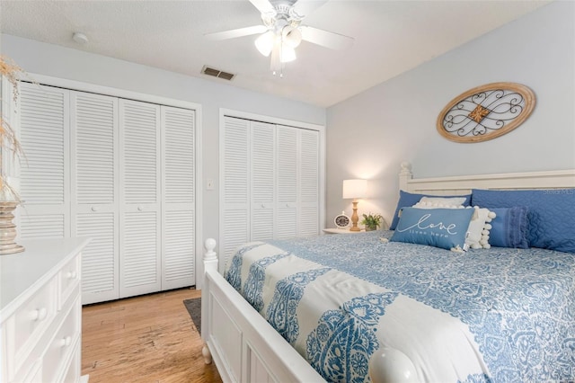 bedroom with ceiling fan, light hardwood / wood-style flooring, and two closets