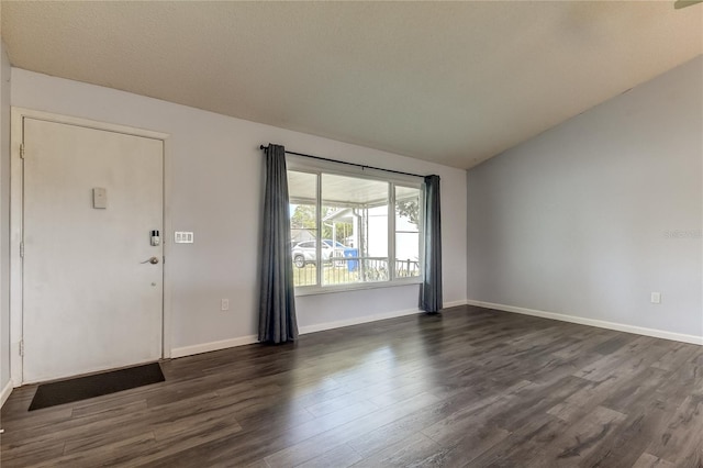 spare room featuring vaulted ceiling, dark wood-style flooring, and baseboards