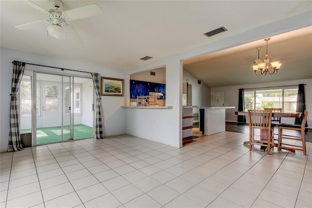 interior space featuring vaulted ceiling, kitchen peninsula, light tile patterned floors, and ceiling fan with notable chandelier