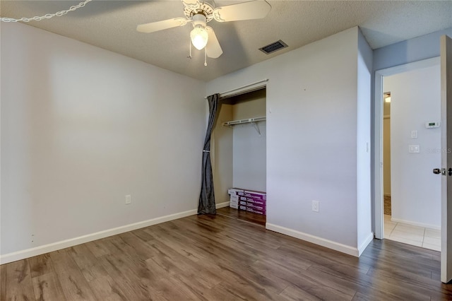 unfurnished bedroom featuring wood-type flooring, a textured ceiling, a closet, and ceiling fan