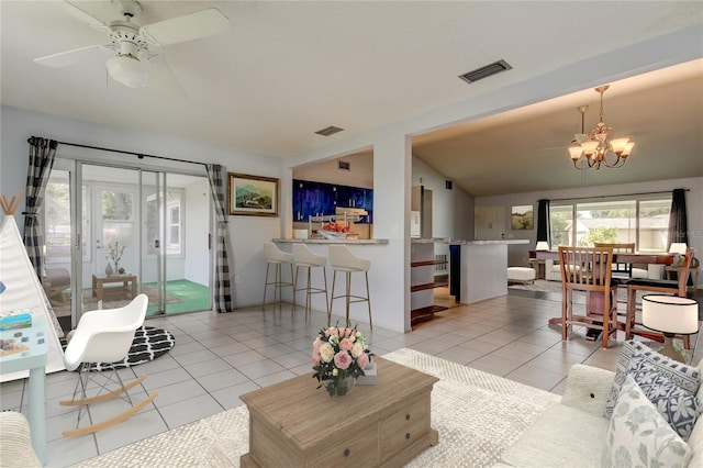 living area featuring ceiling fan with notable chandelier, visible vents, vaulted ceiling, and light tile patterned floors