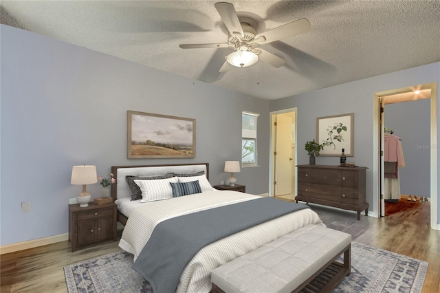 bedroom with a spacious closet, a textured ceiling, baseboards, and wood finished floors