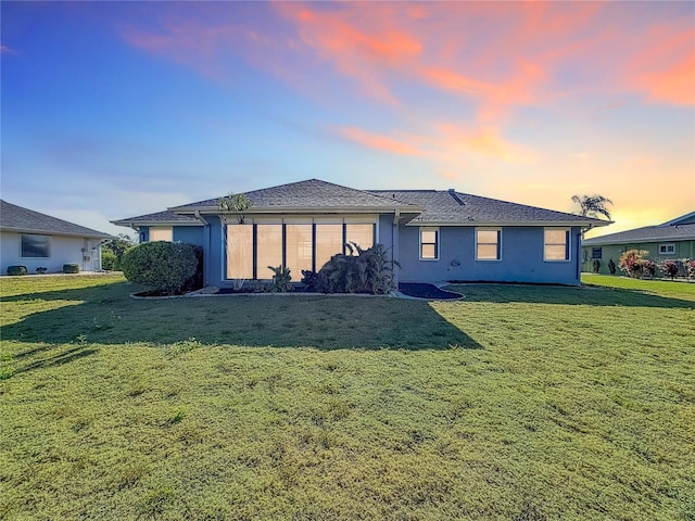 back house at dusk featuring a lawn