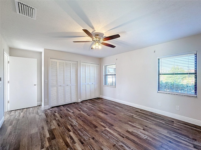 unfurnished bedroom featuring multiple windows, dark hardwood / wood-style floors, and ceiling fan