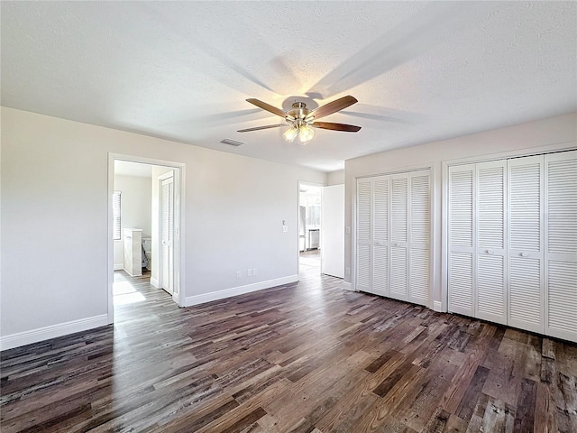 unfurnished bedroom featuring a textured ceiling, two closets, ceiling fan, and dark hardwood / wood-style floors