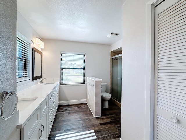 bathroom with hardwood / wood-style flooring, a shower with door, vanity, toilet, and a textured ceiling