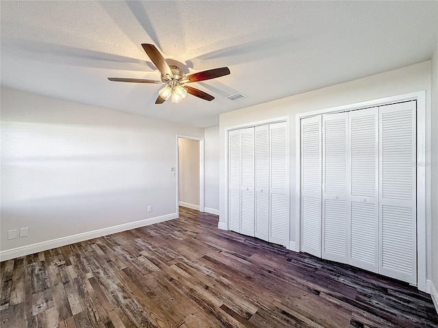 unfurnished bedroom with two closets, ceiling fan, dark hardwood / wood-style floors, and a textured ceiling